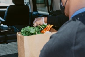 A man with his back to the camera places a bag of groceries into the trunk of an SUV.